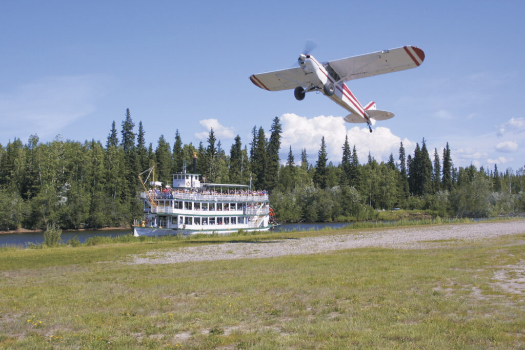 Bush plane flying in front of riverboat Discovery.